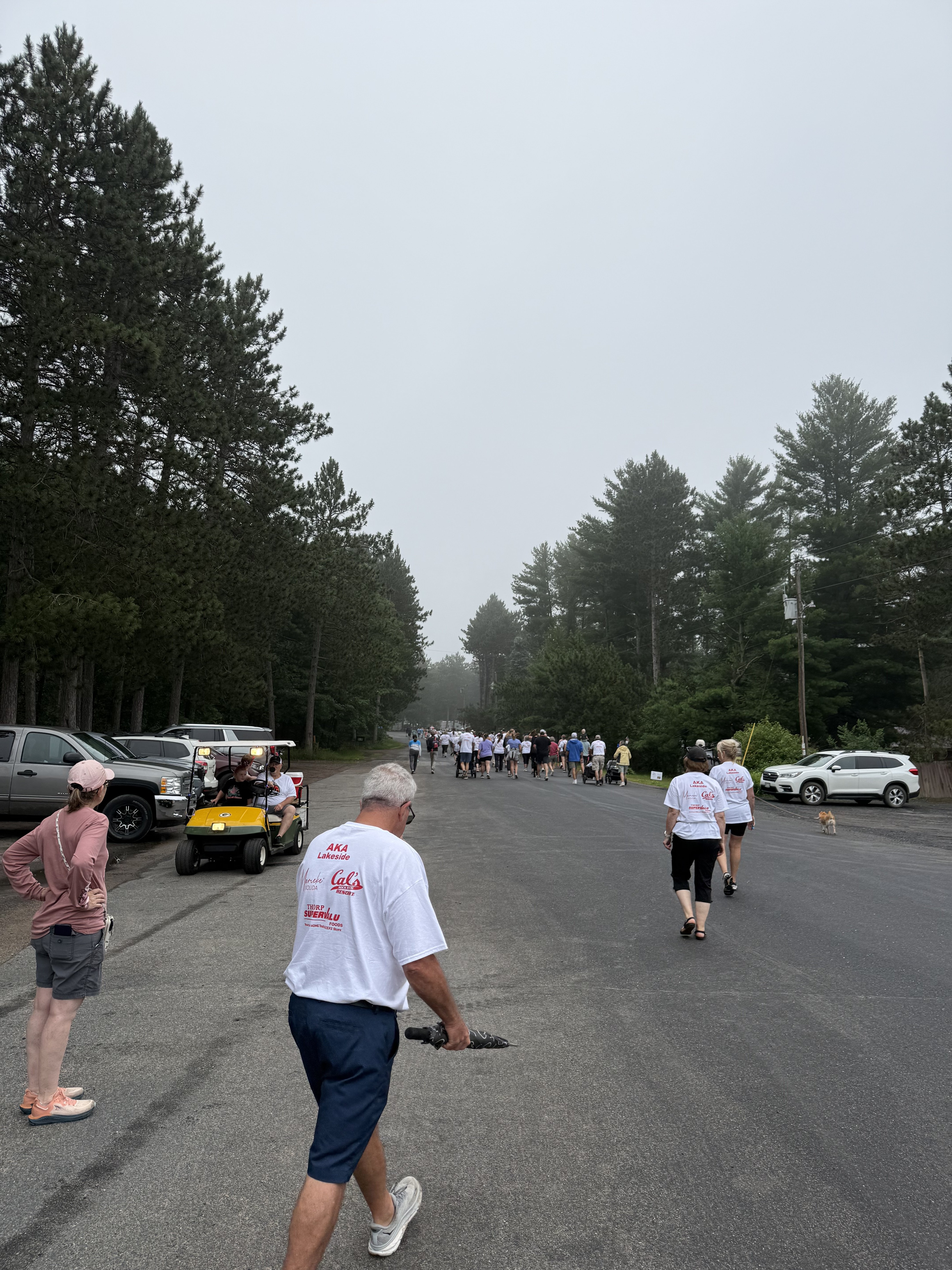 Participants walking on the course wearing sponsor t-shirts with AKA Lakeside, Cal's, and Thorp SuperValu logos