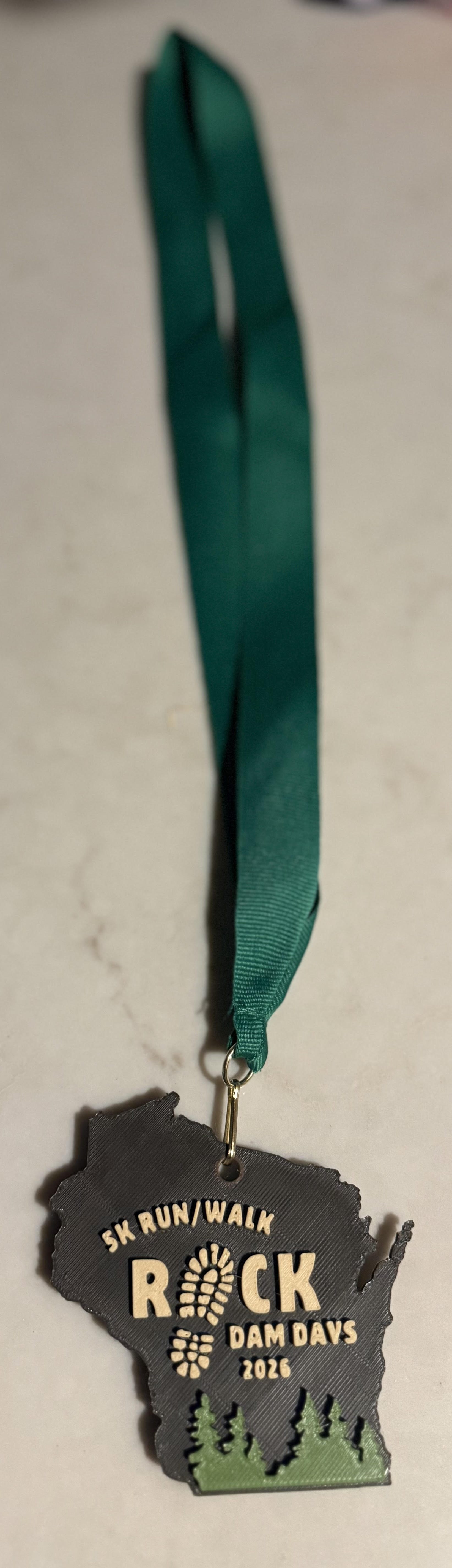 Rock Dam Days 5K 2026 Finisher Medal — Wisconsin state shape with pine trees and forest green ribbon